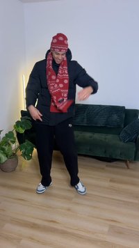 Doudoune noire, écharpe rouge à motifs et bonnet, pantalon de survêtement noir, baskets bleu et blanc. Intérieur avec canapé vert et plantes.