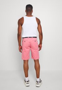 Herrshorts i rosa bomull med avslappnad passform. Har bakfickor, bälteshällor och ett mörkblått bälte. Bärs tillsammans med en vit linne.