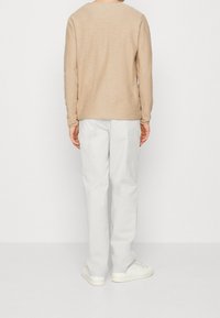 Beige långärmad skjorta med rund hals, matchad med vita byxor. Tyget verkar mjukt och texturerat, med en avslappnad passform.