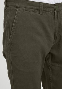 Green cotton chinos featuring a smooth texture, straight fit, side pockets, and a sturdy button closure. Clear stitching detail visible.