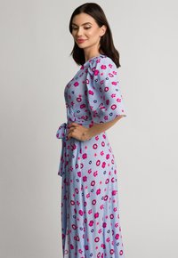 Jasnoniebieska sukienka w kwiaty z lekkiego materiału, z bufiastymi rękawami, związanym w talii paskiem oraz rozproszonymi wzorami różowych i fioletowych kwiatów.