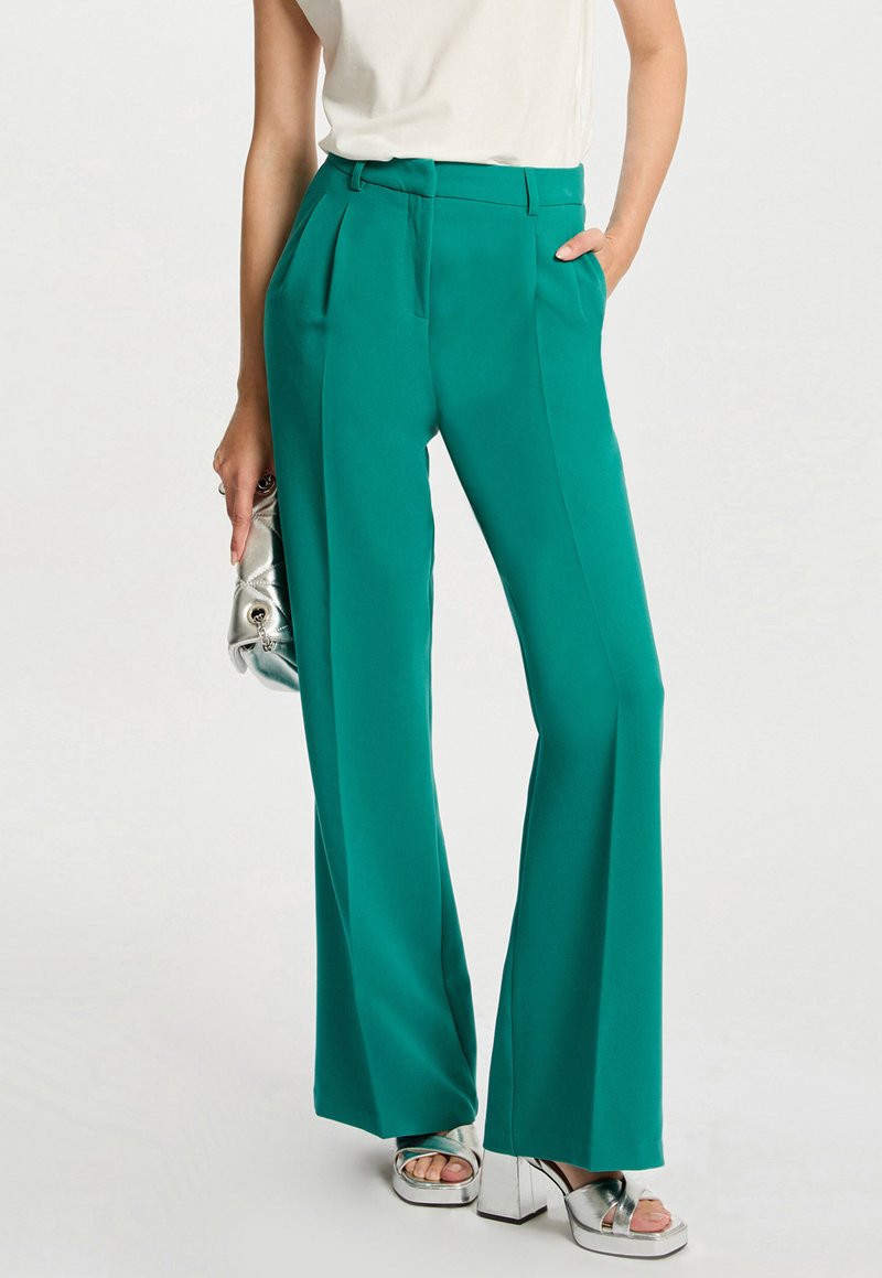 Teal wijde broek gemaakt van een zachte stof, met voorplooien, een hoge taille en zakken, gecombineerd met zilveren platform sandalen.