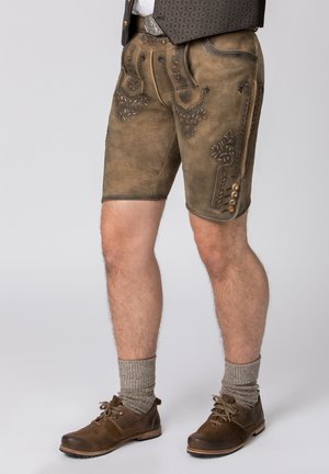 Braune Lederhosen mit filigraner schwarzer Stickerei und dekorativen Knöpfen. Kombiniert mit grauen Kniestrümpfen und braunen Schuhen.