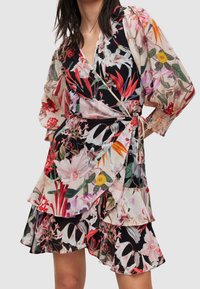 Robe portefeuille florale en tissu transparent, arborant des teintes vives de rouge, rose et noir. Ourlet volanté et manches longues avec poignets élastiques. Liens à la taille.