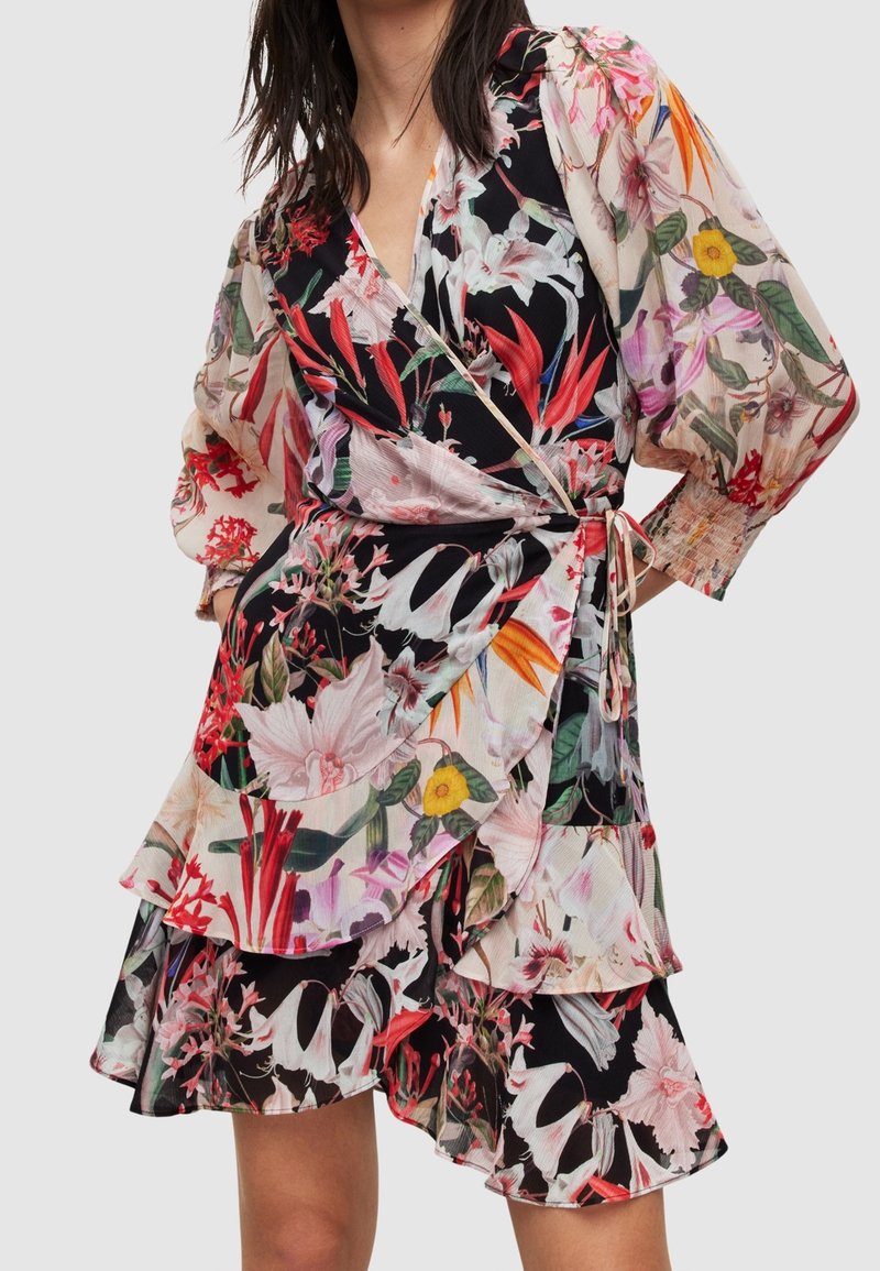 Robe portefeuille florale en tissu transparent, arborant des teintes vives de rouge, rose et noir. Ourlet volanté et manches longues avec poignets élastiques. Liens à la taille.