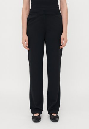 Black, straight-leg trousers made of smooth fabric. Features a mid-rise waist and side pockets, worn with black, rounded ballet flats.
