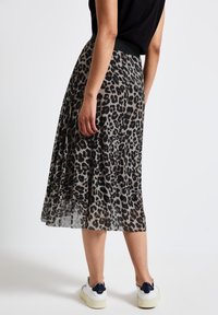 Gonna midi plissettata in tessuto trasparente con stampa leopardata; presenta una vita alta nera e abbinata a sneakers bianche.