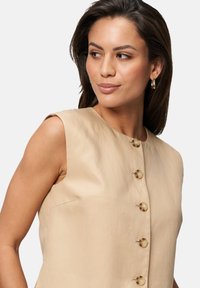 Robe sans manches beige présentant une coupe droite, une fermeture à boutons sur le devant avec des boutons ronds et une texture de tissu lisse.