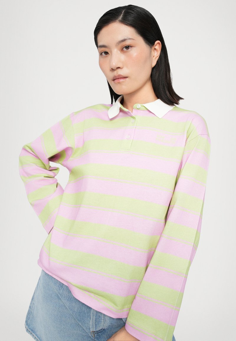 Polo rayé en rose clair et vert, à manches longues, avec un col blanc et des boutons au niveau du col. Texture en coton douce.