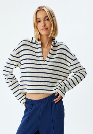 Sweatshirt court en tricot crochet crème avec des rayures marine, doté d'un col plat et d'une coupe loose, associé à un pantalon bleu taille haute.