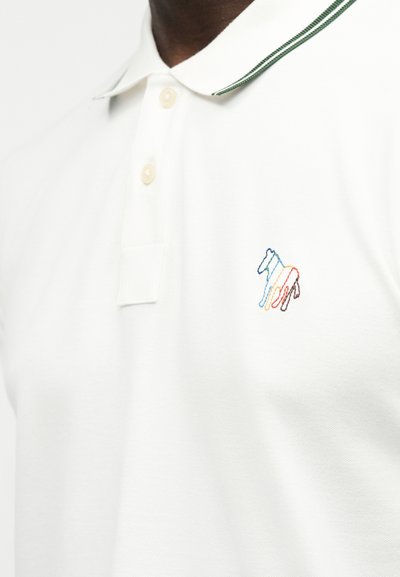 Λευκό πόλο μπλουζάκι με δύο κρέμ κουμπιά και μια μικρή πολύχρωμη κεντημένη ζέβρα στο αριστερό στήθος.