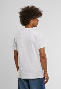 Hvid kortærmet T-shirt lavet af bomuld. Rund halsudskæring, afslappet pasform. Bæres med løse blå denimshorts. Glat tekstur.
