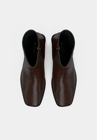 Paire de bottines en cuir marron foncé avec bouts carrés et fermetures éclair latérales, vues de dessus sur un fond blanc.