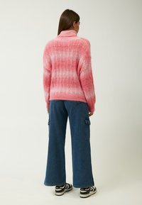 Roze en witte gestreepte chunky gebreide trui met een hoge kraag, fleece-structuur en verlaagde schouders, gecombineerd met brede blauwe denim cargo-broeken.