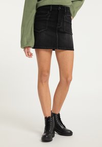 Sort denim mini skirt med frontlommer, en struktureret pasform og rå kant, parret med sorte snørebåndankelstøvler. Lange grønne sweaterærmer.