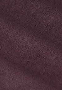 Nahaufnahme eines weichen, strukturierten Stoffes in Dunkelpurpur mit subtilen Falten und einer leicht unebenen Oberfläche.