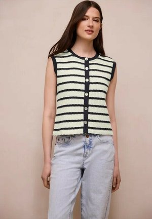 Mujer con camiseta sin mangas de rayas horizontales negras y blancas con botones, combinada con vaqueros de tiro alto azul claro, sobre un fondo liso.