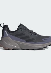 Černá sportovní bota s texturovaným svrškem, materiálem GORE-TEX, gumovou podešví a šedými akcenty. Na boku má tři černé pruhy.