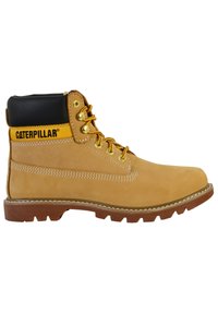 Botte de travail en cuir tan avec un col rembourré noir, accents jaunes, œillets dorés et semelle en caoutchouc robuste avec des crampons profonds pour une meilleure traction.