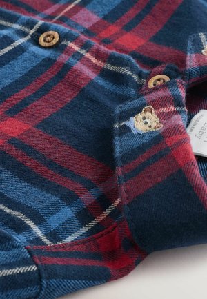 Károvaná košeľa vo námorníckej modrej, červenej a modrej flanelovej farbe. Obsahuje drevené gombíky a vyšívaný detail medveďa na golieri. Mäkčená textúra.
