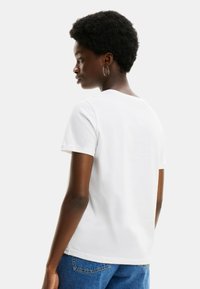 Camiseta de algodón blanca con cuello redondo y mangas cortas, combinada con unos vaqueros azul de talle alto. La tela parece suave y lisa.