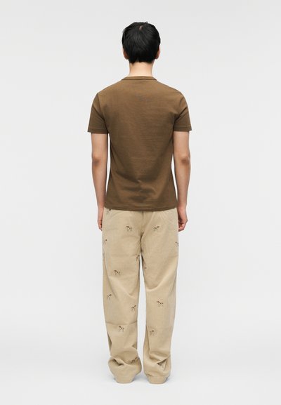 Καφέ βαμβακερό μπλουζάκι σε συνδυασμό με μπεζ παντελόνι κοτλέ με κεντημένα σχέδια ζώων, από την πίσω πλευρά.