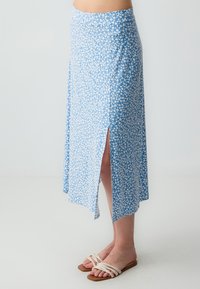 Jupe florale bleu clair avec une fente sur le côté, fabriquée dans un tissu doux. Présente un motif de fleurs blanches délicat, longueur cheville avec une silhouette en A.