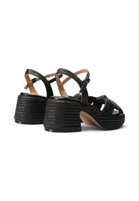Sandali platform neri con tacco a texture intrecciata, cinturino alla caviglia regolabile e design annodato sulla parte superiore. Accenti in pelle liscia.