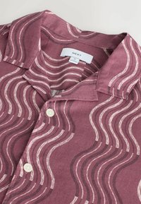 Chemise mauve à manches courtes avec motif à rayures ondulées beige et brun foncé, boutons blancs, et étiquette de marque "NEXT" taille M.