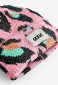 Rozā filca beanie ar melnu leopardu rakstu un piparmētru zaļām, persiku akcentiem. Iezīmēta ar baltu birku ar melnu tekstu no vienas puses.