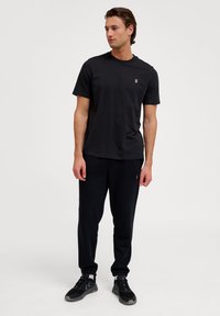 Zwarte katoenen t-shirt met ronde hals en korte mouwen, gecombineerd met zwarte sweatpants. Beide kledingstukken hebben een relaxte pasvorm en een minimalistisch ontwerp.