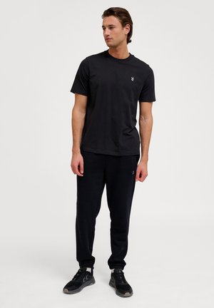 Zwarte katoenen t-shirt met ronde hals en korte mouwen, gecombineerd met zwarte sweatpants. Beide kledingstukken hebben een relaxte pasvorm en een minimalistisch ontwerp.