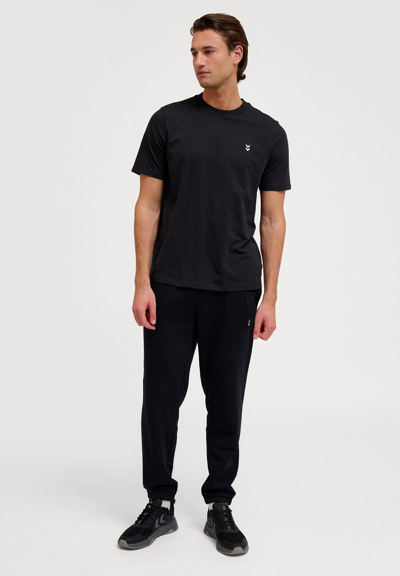 Zwarte katoenen t-shirt met ronde hals en korte mouwen, gecombineerd met zwarte sweatpants. Beide kledingstukken hebben een relaxte pasvorm en een minimalistisch ontwerp.
