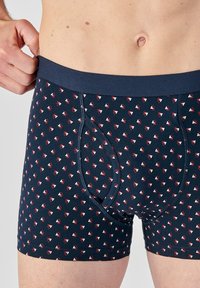 Boxer shorts blu navy realizzati in tessuto morbido, con un motivo triangolare ripetuto in rosso e bianco. Vita elastica per il comfort.