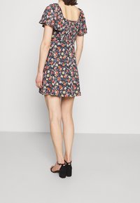 Vestido floral con fondo marino, escote cuadrado, mangas cortas con volantes y cintura entallada. Sandalias de tacón alto negras.