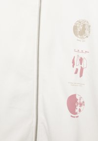 Bílá zipová bunda s růžovými grafikami, včetně kruhů a abstraktních tvarů, s textem „Od roku 1991“ a hladkou texturou látky.