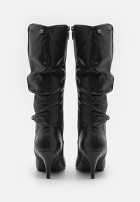 Black leather knee-high boots with a slouchy design, pointed toe, and 4-inch stiletto heel. Features dual zippers and a signature accent.