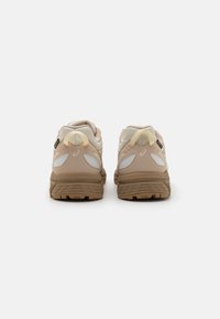 Μπεζ αθλητικά παπούτσια με υφή στην επάνω πλευρά, πάνελ από διχτυωτό υλικό και ανακλαστικές λεπτομέρειες. Παχιές λαστιχένιες σόλες με καθορισμένο σχέδιο πέλματος.