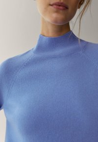 Pull bleu clair avec un col montant, texture côtelée et manches raglan. Le tissu semble doux et ajusté, mettant en valeur un joli détail de tricot.