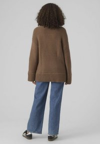 Brun chunky stickad tröja med ribbad nederkant och manchett, bärs med vida blå denimjeans och svarta sneakers. Texturerad tygdetalj synlig.