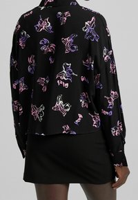 Black floral blouse with purple and pink abstract patterns, long sleeves, and relaxed fit, paired with a fitted black skirt.