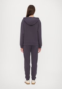Mörklila huvtröja och matchande sweatpants i ett mjukt tyg. Har huva, ribbade ärmslut och en avslappnad passform med en slät yta.