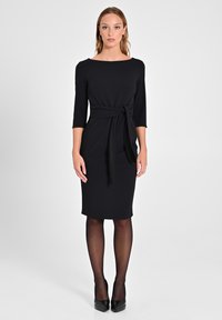 Schwarzes knielanges Kleid mit Dreiviertelärmeln, einem Bootsausschnitt und einer gebundenen Taille. Hergestellt aus glattem Stoff mit einer figurbetonten Silhouette.