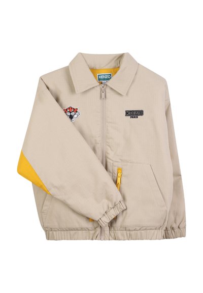 Veste zippée beige avec un accent jaune sur la manche, portant un logo de tigre et "KENZO PARIS" brodé sur la poitrine. Poignets élastiques.