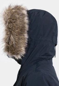 Navy parka dengan tudung berlapik bulu. Bulu tersebut berwarna coklat muda dan berbulu lebat. Fabriknya kelihatan licin dan tahan air, dengan bentuk tudung yang terstruktur.