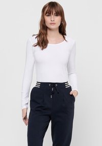 Langärmliges weißes Oberteil mit rundem Ausschnitt, kombiniert mit marineblauen Jogginghosen, die über einen Kordelzug und gestreifte Akzente am Bund verfügen.