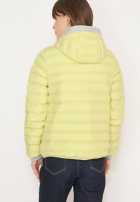 Doudoune jaune à capuche, avec des sections matelassées et un col gris. Fabriquée en matériau léger, elle présente une coupe décontractée.