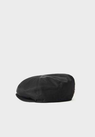 Casquette plate noire avec des panneaux cousus et une courte visière, présentée sur un fond gris clair uni.