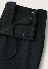 Pantalon noir à fines rayures avec une taille ouverte dotée d'un bouton, d'une fermeture éclair et d'un cordon noir pour un ajustement réglable.