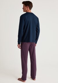 Navy long-sleeve top paired with burgundy patterned pajama pants featuring white and blue dots; smooth fabric with a relaxed fit.